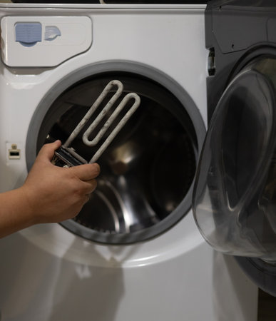 A man examines a heating element with scale against the background of a washing machine. The washing...