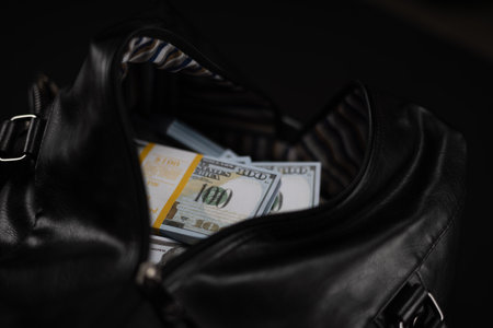 Close-up of an open bag full of money on a black background. New packs of one hundred dollar bills...