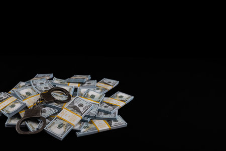 On a black background, handcuffs lie on a pile of money. Copy space. Place for an inscription. A lot of money is piled in a big pile and on top are heavy metal handcuffs.の写真素材
