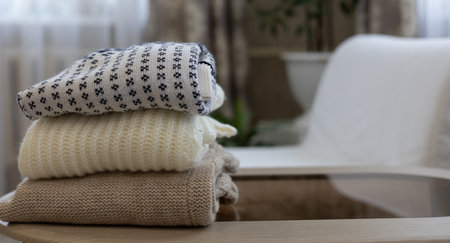 A stack of knitted clothes is folded on a table in the living room. Dismantling the closet from old,...