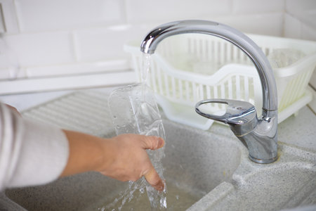 A woman rinses plastic bottles in the kitchen before sending them for plastic recycling. A woman...