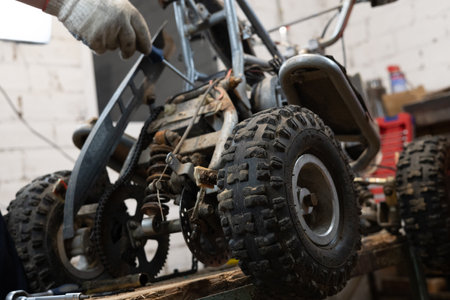 A man finishes repairing an ATV in his garage. A man repaired his sons little red four-wheeler in his garage and replaced the broken parts with new ones. Broken quad bike concept.の写真素材