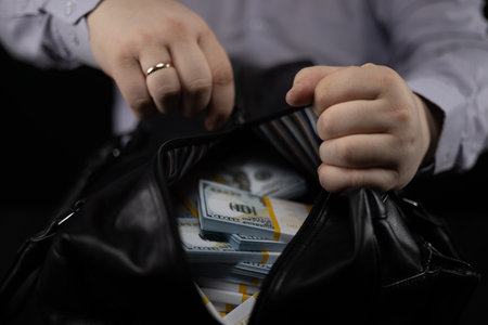 A man unzips a large bag with bribe money on a black background. A man in business attire received a...