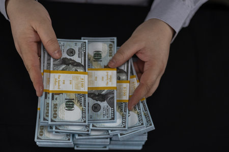 View from above. Hands holding stacks of hundred dollar bills close-up on a black background....