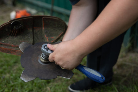 In the summer, a man is repairing a grass trimmer in his yard. Repairing a grass trimmer close-up on...