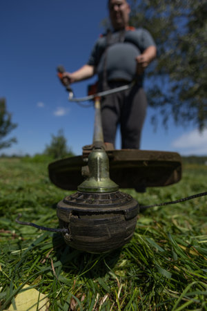 Vertical. On a clear day, a man mows the grass in his backyard with a trimmer. Hold the trimmer...