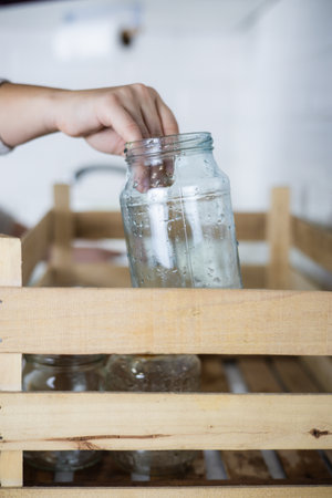 Vertical. A housewife reaches out and places an old glass jar in a recycling bin. A housewife collects unwanted glass jars and bottles at home to send for recycling. Glass recycling concept.の写真素材