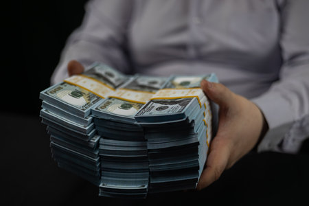A businessman places stacks of dollars on the table in front of him. A man places stacks of hundred...