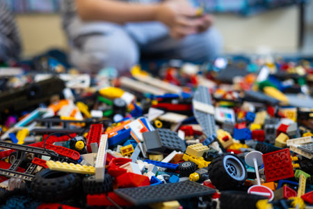 There are a large number of parts lying on the floor, and a child is sitting in the background. A child in a childrens room plays with and collects different toys.の写真素材