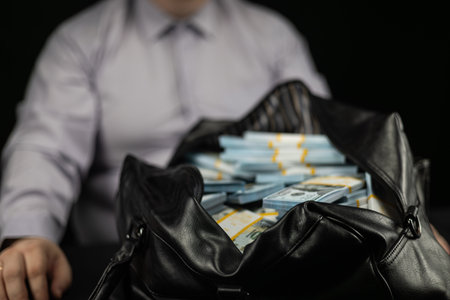 A man in a white shirt sits in front of a bag full of dollars. Businessman with a bag full of stacks...