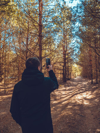 A man takes a photo of a beautiful forest road on his phone. While walking through the forest, the...