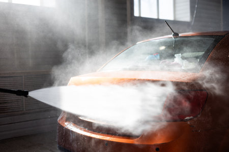 A beautiful orange car is sprayed with a strong stream of water from a high-pressure gun at a car wash. Appearance care. A man came to wash his bright orange car.の写真素材