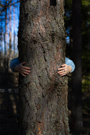 Standing behind a tree, a woman hugs him with her arms. A woman activist is fighting to save the...