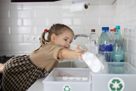 A child pulls a small hand with a plastic bottle to put it in a recycling box. A child in the...
