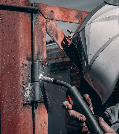 A man in a protective mask works as a welder, securing hinges on a gate. While welding new hinges on...