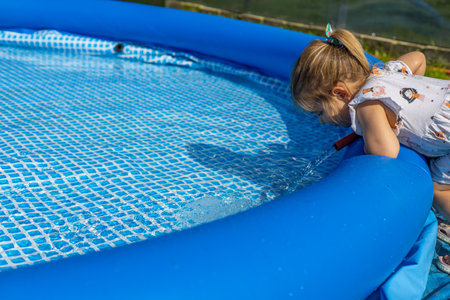 A child pours water from a hose into the pool. On a sunny summer day in the backyard, a child fills...
