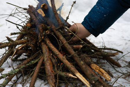 In the forest, a man makes a fire by setting dry firewood on fire to keep warm. A man is engaged in...