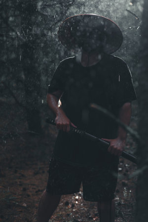 A samurai warrior stands in a rainy forest holding a katana. The dark atmosphere highlights the strength and skill of the samurai with the katana. Raindrops fall around the man with the katana.の写真素材
