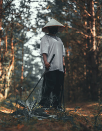 A confident warrior in traditional Japanese attire holds a katana in a dense forest, the sunlight filtering through the trees adds a sense of mystery and danger. Warrior with a katana.の写真素材