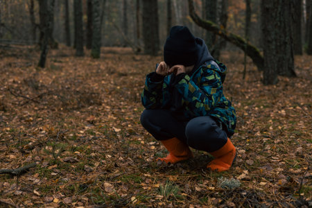 Lost child squatting and crying in a forest while wearing orange boots, covering face with hands,...