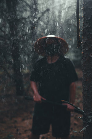 A man in a samurai cosplay stands in the rain with a katana in a dark forest radiating strength and honor. A man in a samurai costume with a katana stands in the forest in the rain.の写真素材