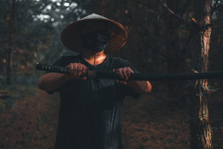 A samurai warrior in the forest draws his katana with concentration and courage, embodying Japanese martial arts. The blade of the katana sparkles with power in the dark, gloomy atmosphere.の写真素材