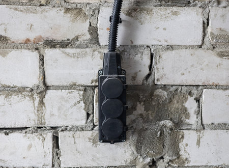 Triple outlet on brick wall in barn. Outlet on wall. Black triple industrial outlet hanging on white...