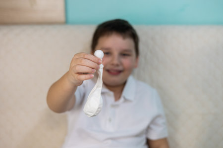 A smiling child practices autoinsufflation using a nasal balloon to equalize pressure in the ear, a method to relieve ear discomfort. Doctors appointment at home.の写真素材