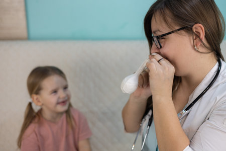 A pediatrician shows a smiling girl how to use a nasal blower correctly, and also explains how to clean her ears and maintain their health at home. The doctor examines the child at home.の写真素材