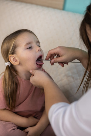 Vertical. A pediatrician examines a young child at home, checking the throat for signs of illness....
