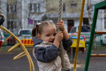 A girl child climbs a rope on a playground, enjoying outdoor activities, developing strength and coordination. Smiling and playing, the child personifies the joy of an active childhood.の写真素材