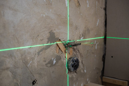 Green laser level projects straight horizontal and vertical lines onto concrete wall during home renovation, providing accurate measurements for electrical work. Laser level alignment.の写真素材