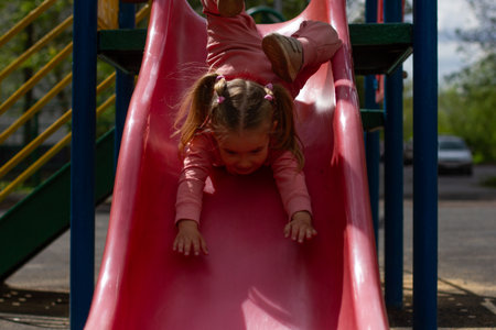 The child has fun rolls from the slide on the site. A happy little girl, first gliding along a slide...