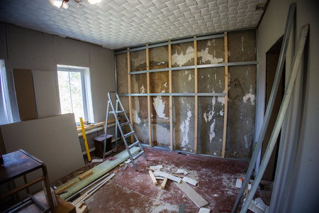 Metal frame attached to the wall with wooden bars and screws, preparing for plasterboard installation in a renovated room with scattered construction materials and a nearby ladder.の写真素材