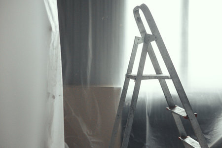 Sunlight filters through sheer curtains, casting a soft glow on a metal ladder in a minimalist room. The scene evokes themes of renovation and simplicity in a serene space.の写真素材