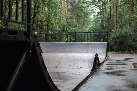 The concrete ramp skate is ready for action in a calm park surrounded by lush greenery and a metal fence, creating an ideal place for lovers of city sports. Bolshoi ramp in Skate Park.の写真素材