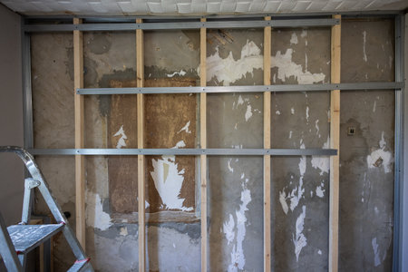 Metal and wood studs are attached to a concrete wall to create a frame for a partition during a home renovation project, with remnants of old wallpaper visible. A frame for attaching drywall sheets.の写真素材