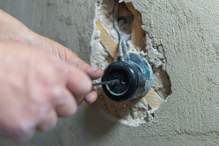 An electrician uses a screwdriver to tighten screws on an electrical outlet during renovation work on a home under construction, ensuring safety and functionality. An electrician installs an outlet.の写真素材