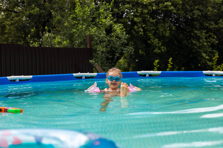 Young girl wearing goggles and armbands enjoying a sunny day while relaxing in a backyard...