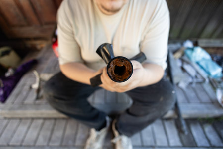 Man demonstrating a section of an old water pipe revealing extreme rust and mineral buildup, indicating severe corrosion and a major blockage impacting water flow and plumbing system efficiency.の写真素材