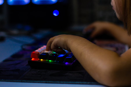 A childs hands actively interact with a vibrant mechanical keyboard with RGB backlighting, highlighting the immersive and dynamic online gaming experience. A child playing on a computer.の写真素材