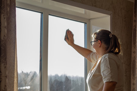 A woman washes a window in a house with a microfiber cloth. The woman is doing housework while...