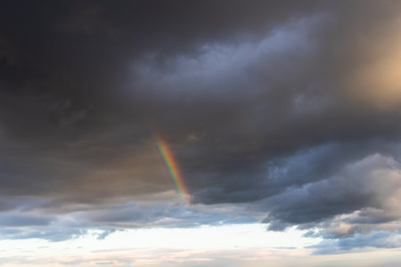 Rainbow in the dark sky with clouds and sun rays, natural backgroundの写真素材