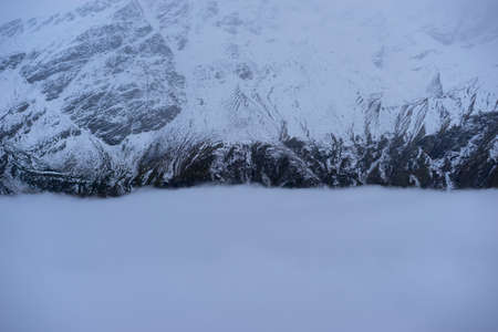 Aerial view of misty mountains at sunrise. Clouds drift amid rocky cliffs.の写真素材