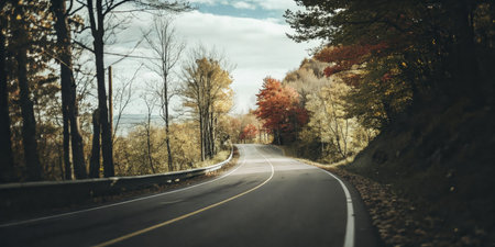 Scenic Winding Road Through Autumn Forest with Vibrant Foliage and Blue Skyの素材