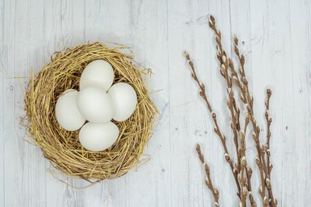white Easter eggs in a nest and a willow on a gray wooden table. the view from the top