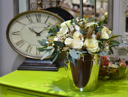 Bouquet of roses in a shiny metal bucket on a green table on the background of mirrors and clocks.の写真素材