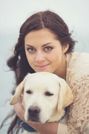 Portrait of beautiful young woman playing with dog on the sea shoreの写真素材
