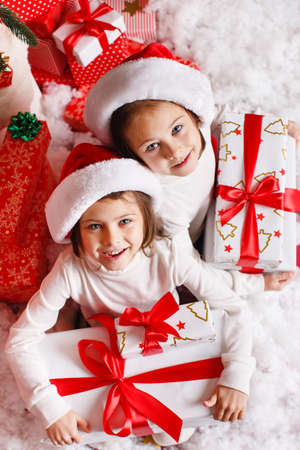 Santa hat Christmas girls holding christmas gifts smiling happy and excited  Cute beautiful santa children on red の写真素材