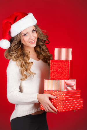 Santa girl holding christmas gift  Young happy woman in santa hat looking sideways showing Christmas present isolated on white Beautiful cute young santa woman の写真素材